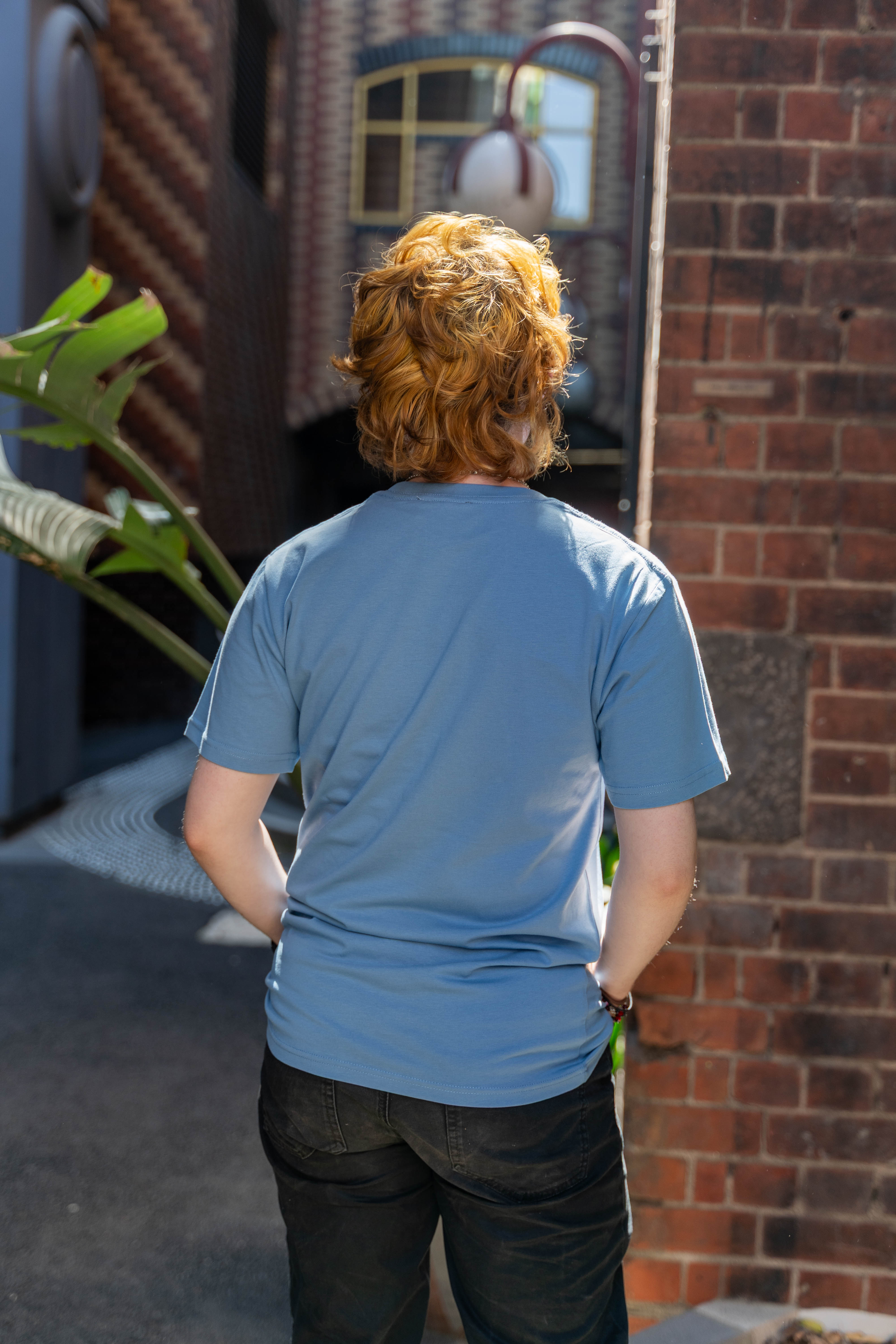 Rear view of a model wearing the limited edition blue Pride Unity Tee from RMIT Store, highlighting the plain back design amidst a vibrant urban setting.